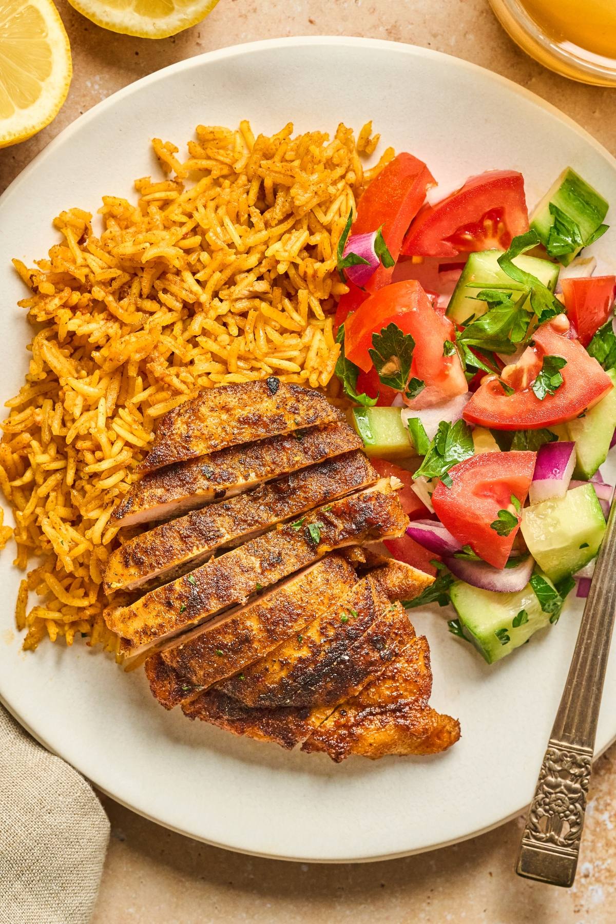 A plate with spiced rice, sliced grilled chicken breast, and a fresh tomato-cucumber salad.