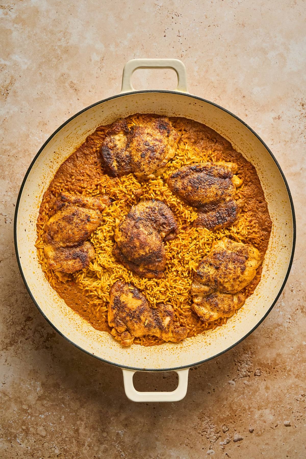 A round pan with baked seasoned chicken thighs on top of golden rice.