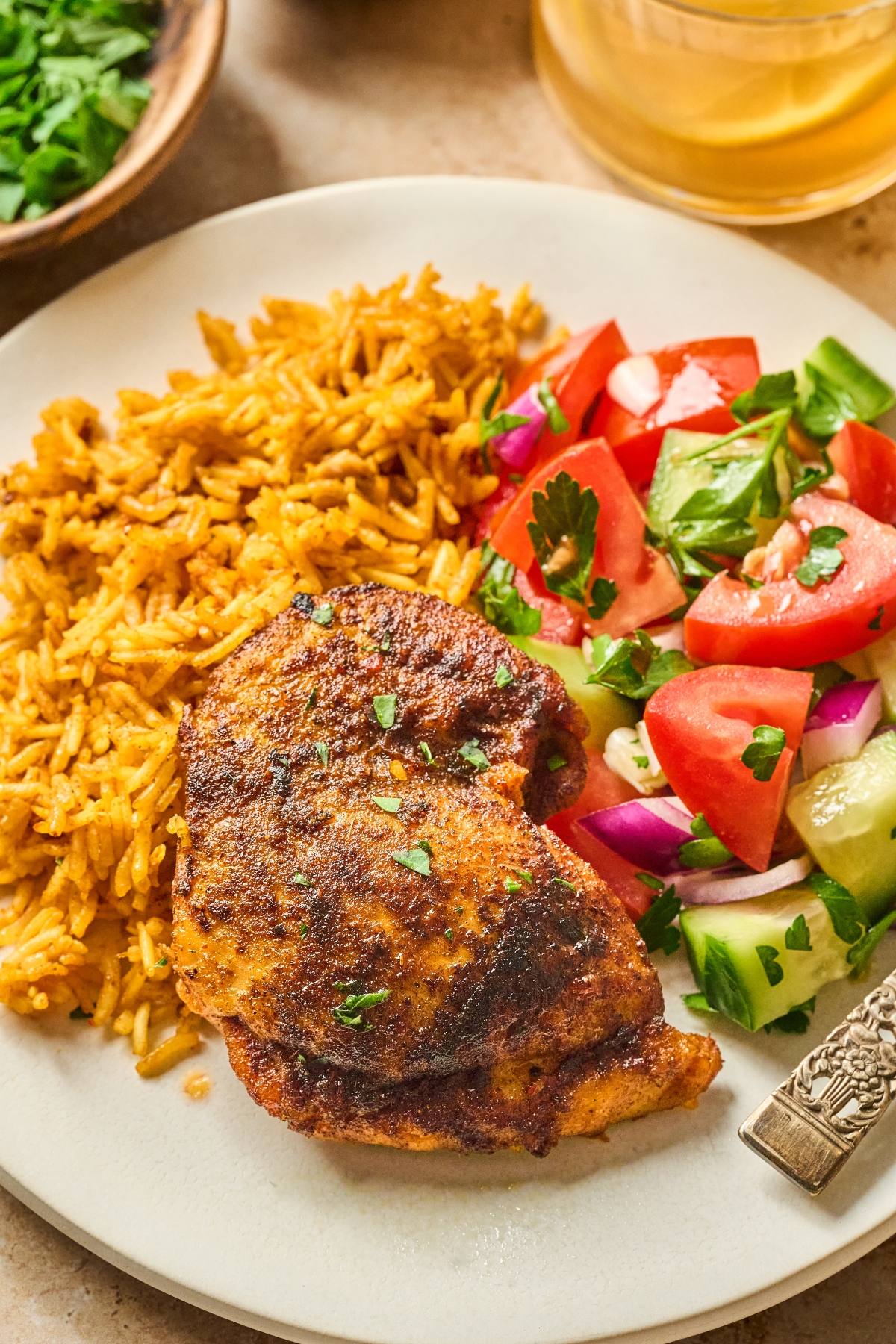 A plate with spiced chicken, yellow rice, and a fresh salad of tomatoes, cucumbers, and red onions.