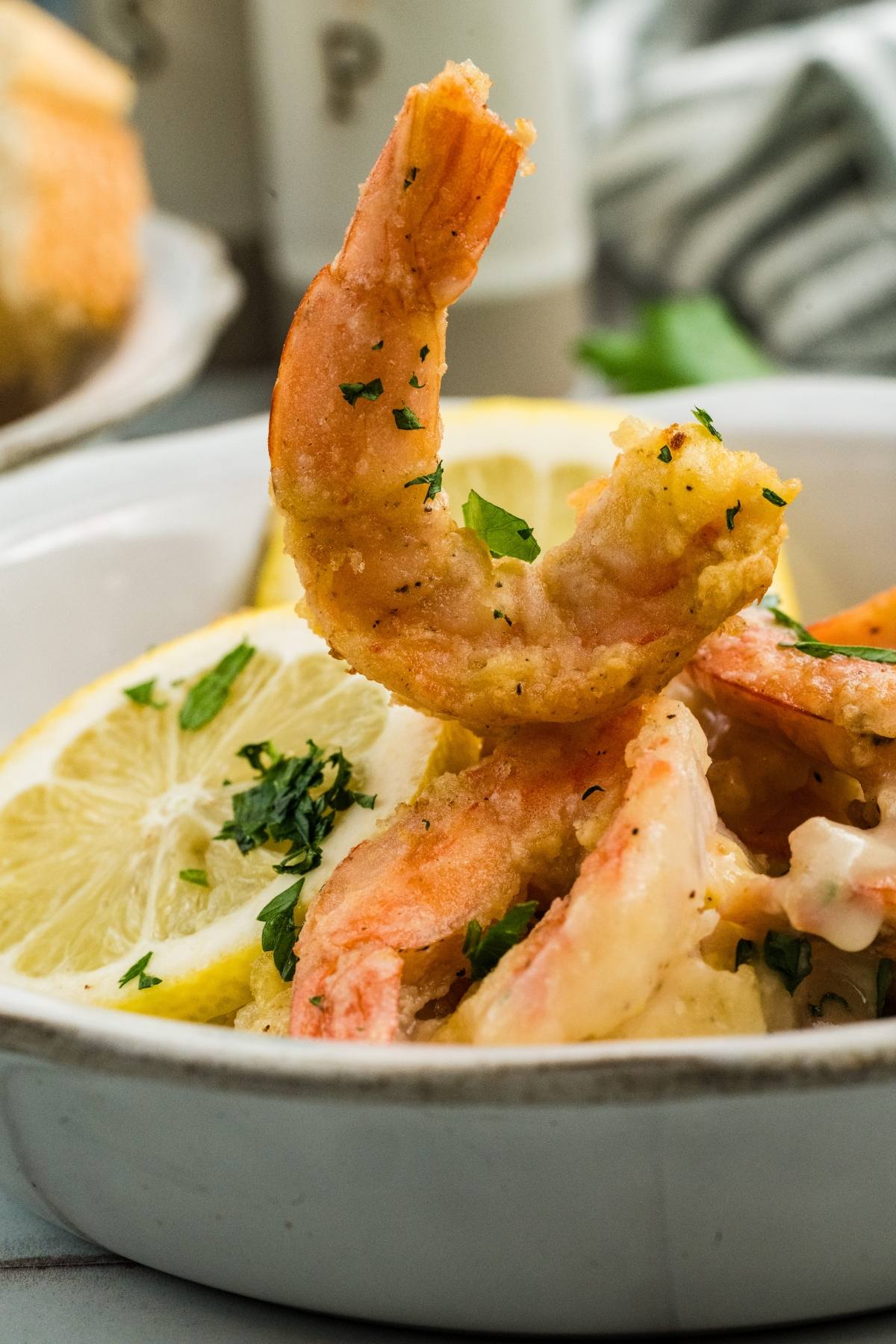 Close-up of seasoned shrimp garnished with parsley, served with lemon slices in a white bowl.