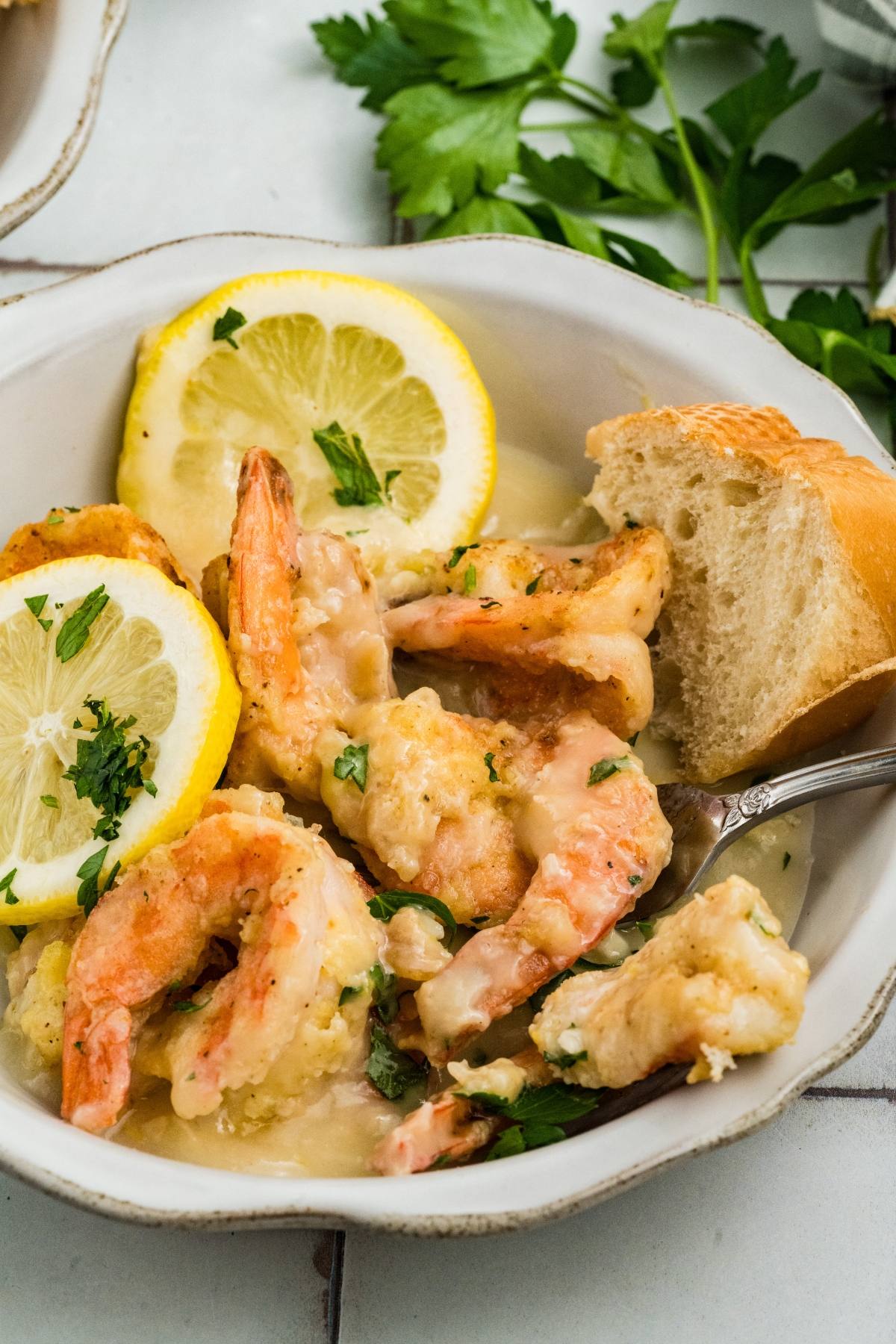 Bowl of shrimp with lemon slices, parsley, and a piece of bread on the side.