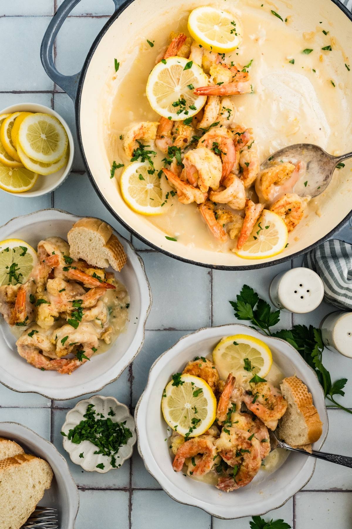 Shrimp in creamy lemon sauce served in a pot and bowls, garnished with lemon slices, parsley, and bread.