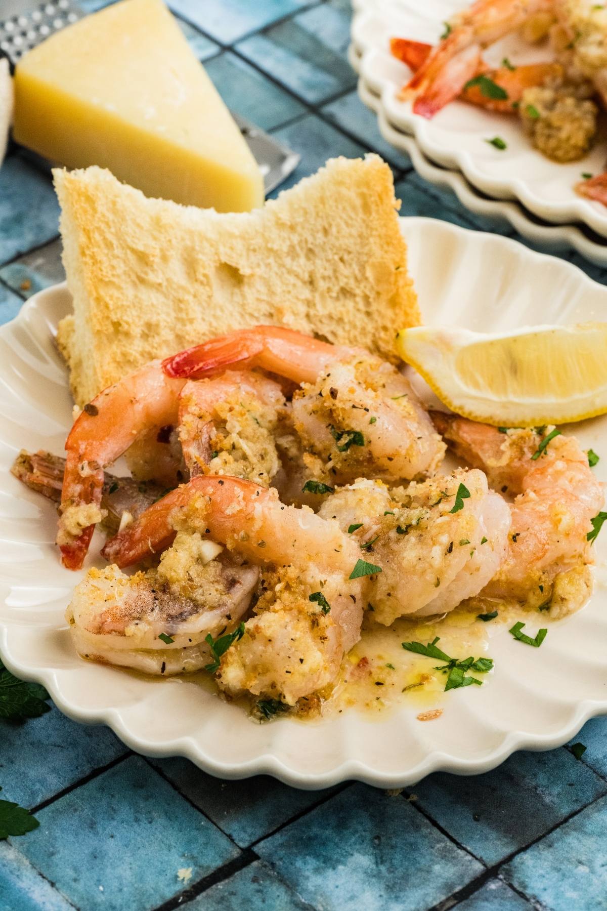 Cooked shrimp with bread, lemon wedge, and parsley on a white plate, on a blue tiled table.