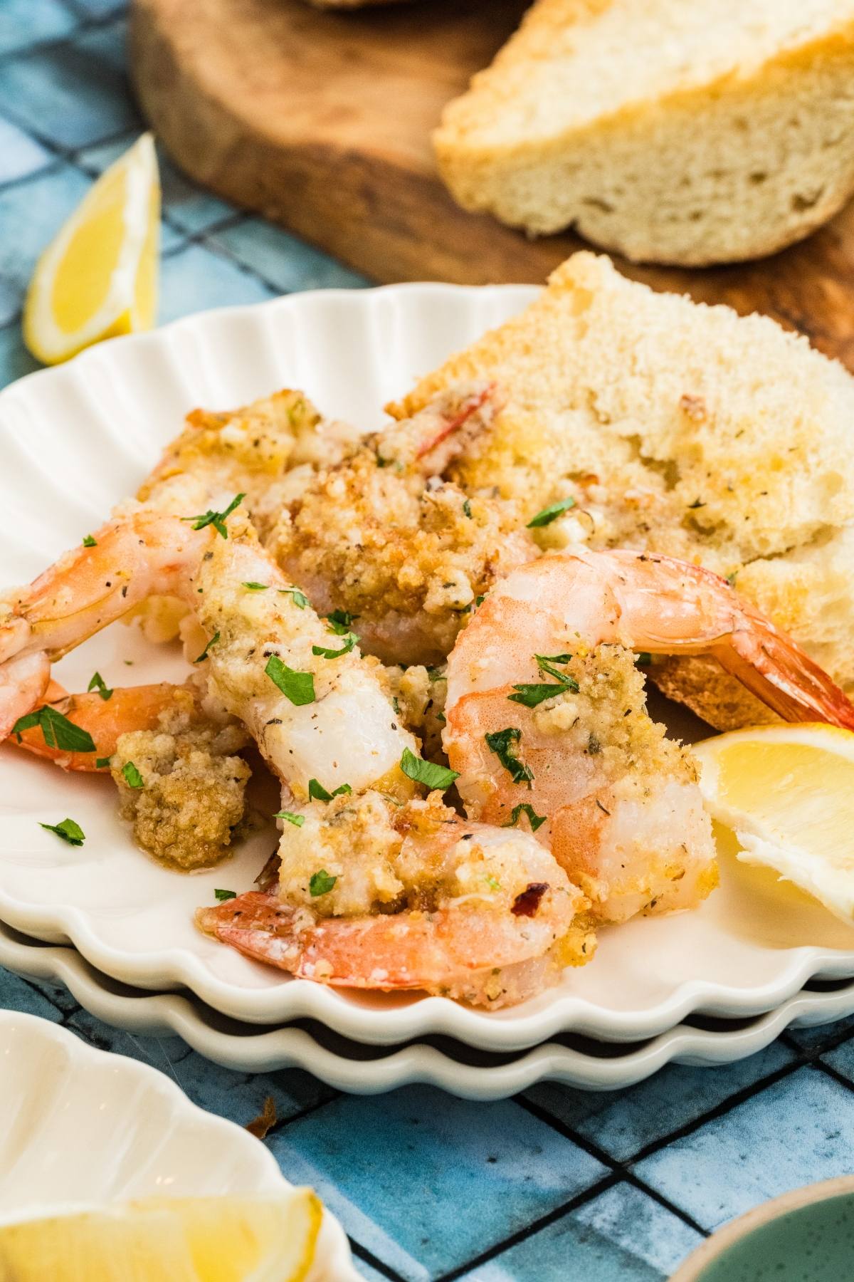 Five baked shrimp with breadcrumbs and herbs served with bread and lemon wedges on a white plate.