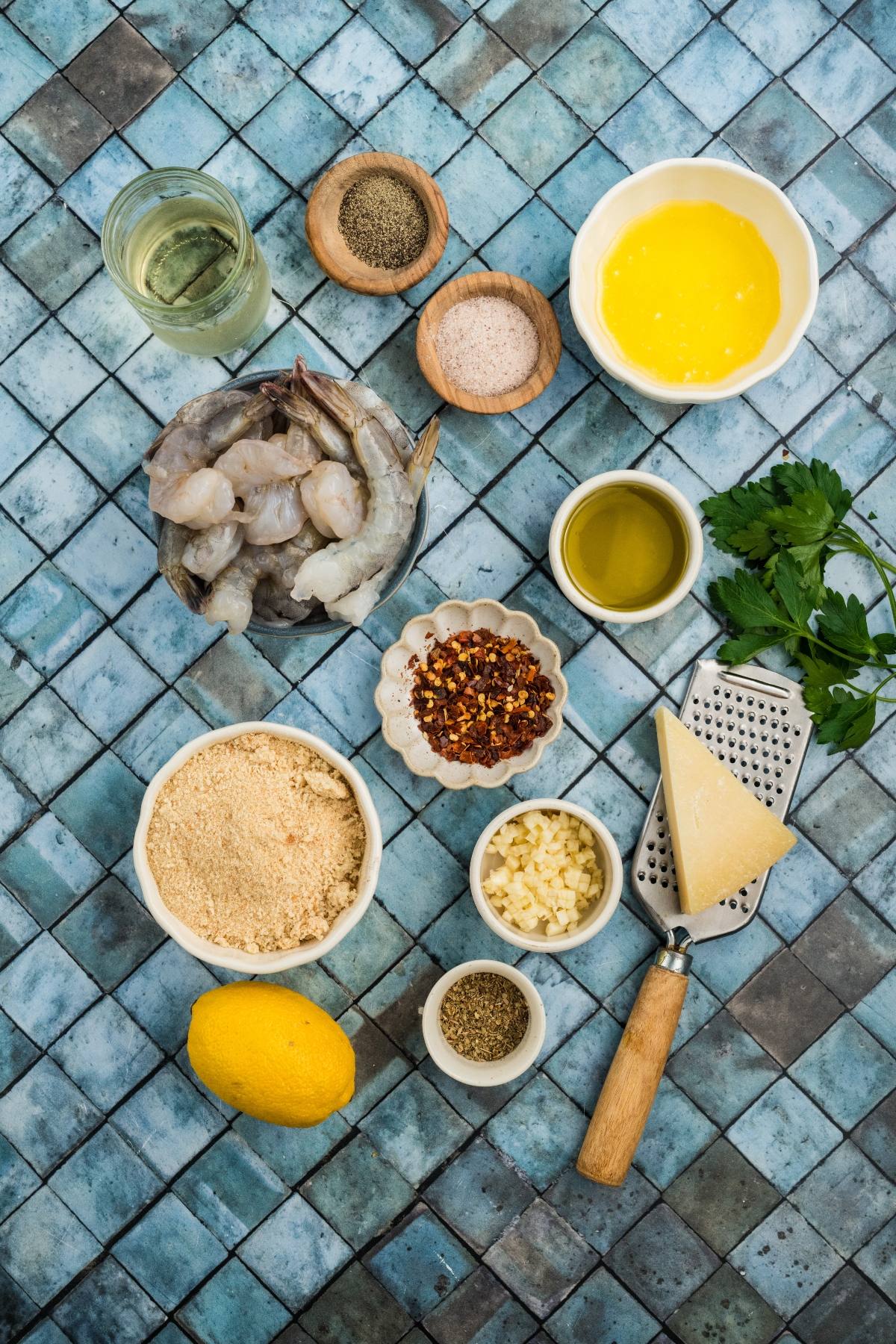 Various ingredients for cooking shrimp displayed on a blue tile surface, including shrimp, lemon, spices, and cheese.