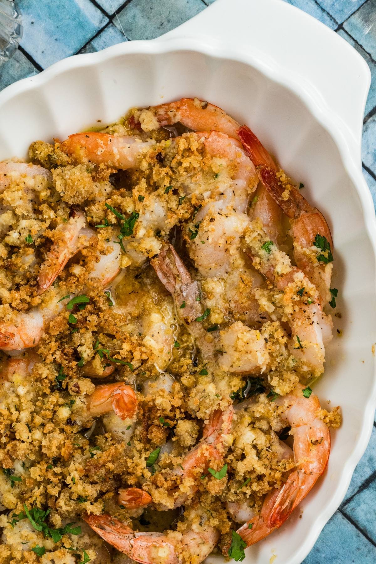 Baked shrimp with golden breadcrumb topping in a white dish, garnished with chopped herbs.