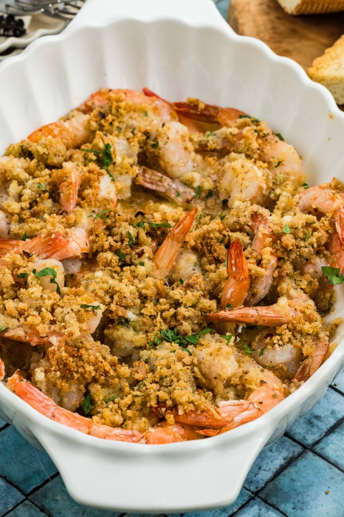 Baked shrimp topped with golden breadcrumb mixture in a white scalloped dish.