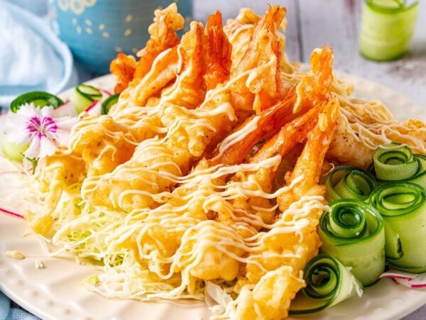 A plate of shrimp tempura is served with a blue cup and a blue mug.