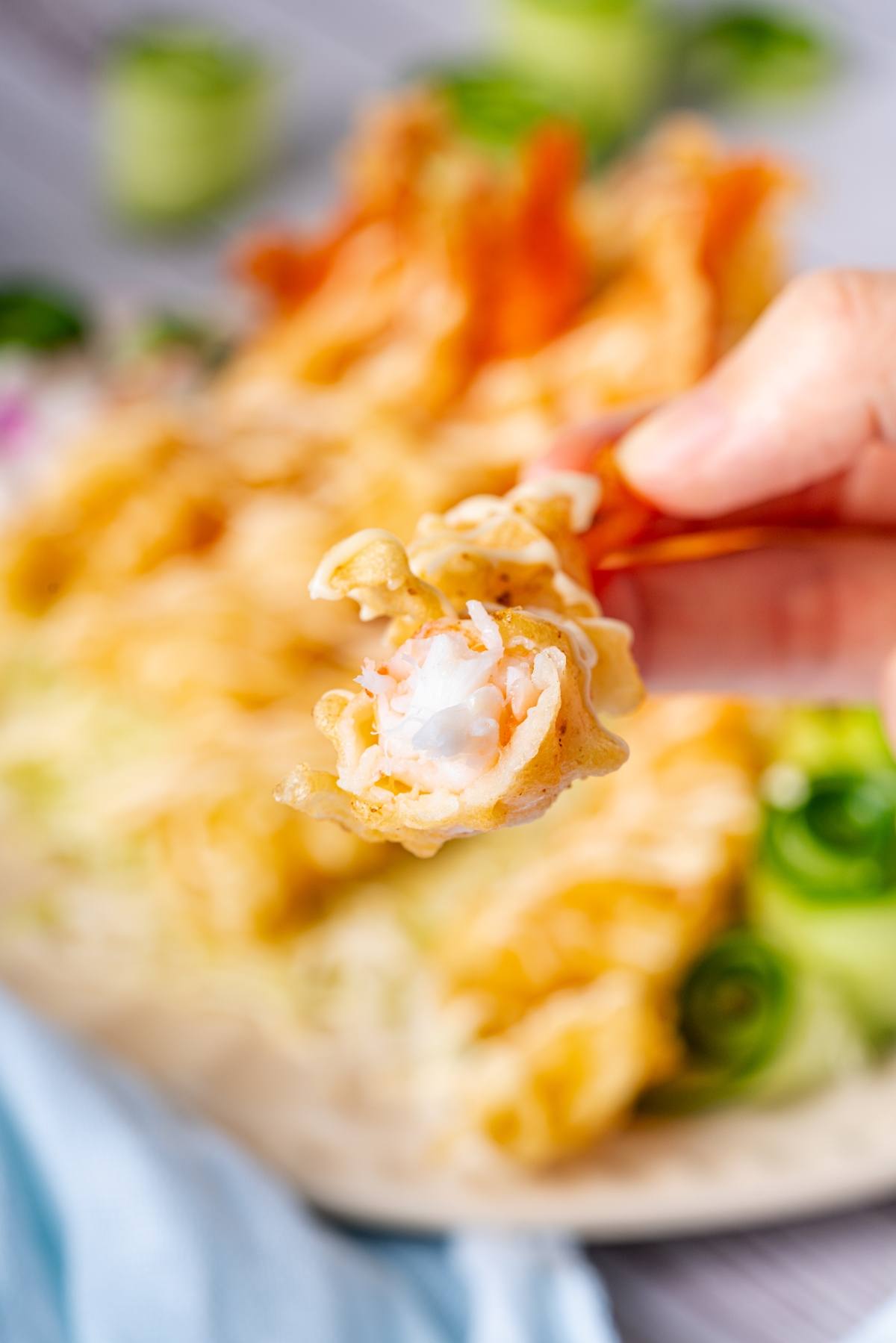 A hand holds a crispy fried wonton with cream cheese filling, with more wontons blurred in the background.