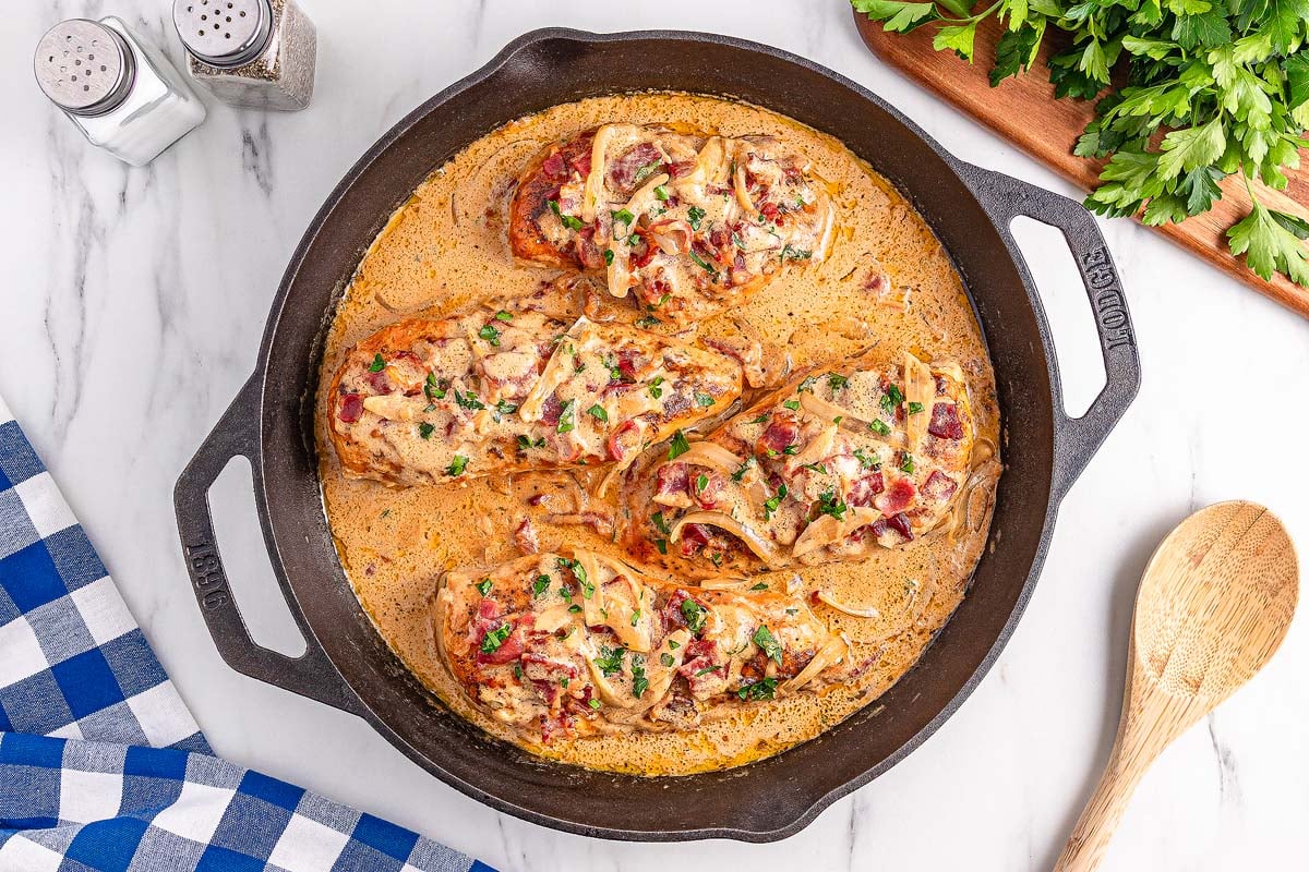 Smothered Chicken breasts in creamy sauce with onions and herbs are cooked to perfection in a cast iron skillet, seen from above.