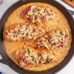 Three cooked chicken breasts in a creamy sauce with onions and herbs, this smothered chicken is served hot in a black skillet atop a marble surface.
