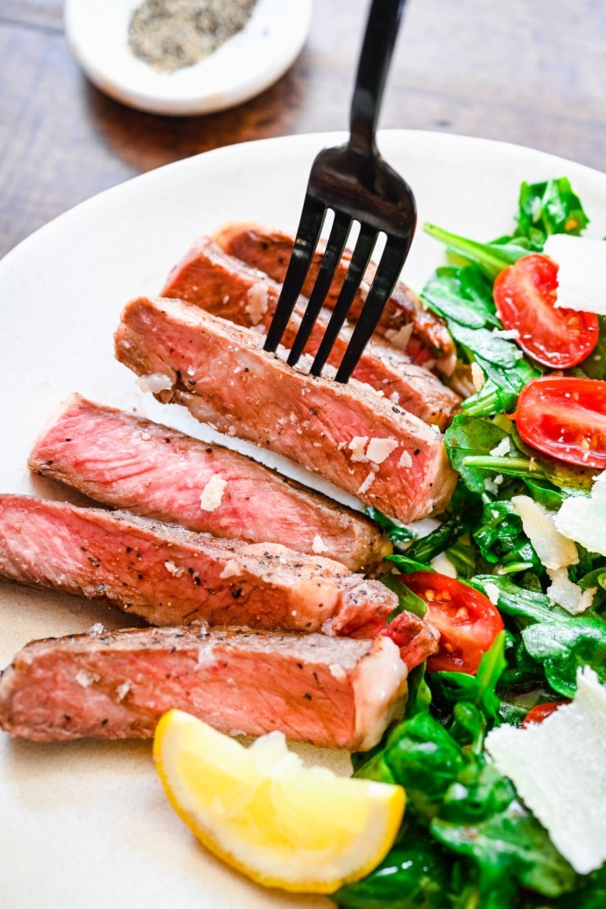 Sliced steak with a fork, served with salad, cherry tomatoes, shaved cheese, and a lemon wedge on a plate—perfect for those looking to try classic Italian dinner recipes.
