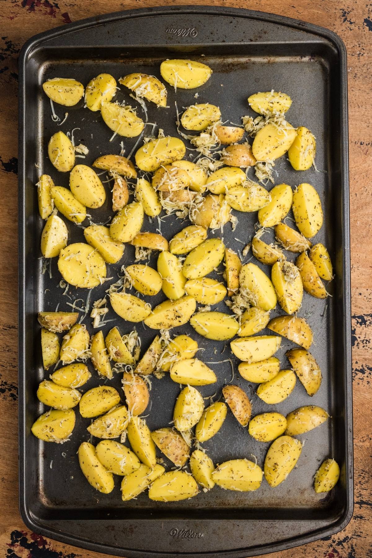 Sliced seasoned potatoes with herbs and cheese on a baking tray, ready for roasting.