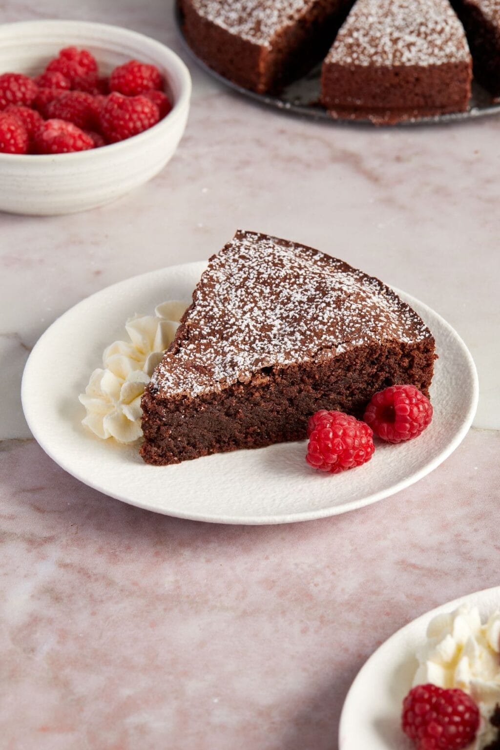 A slice of chocolate cake with powdered sugar, whipped cream, and raspberries on a white plate—perfect inspiration for Italian dessert recipes.