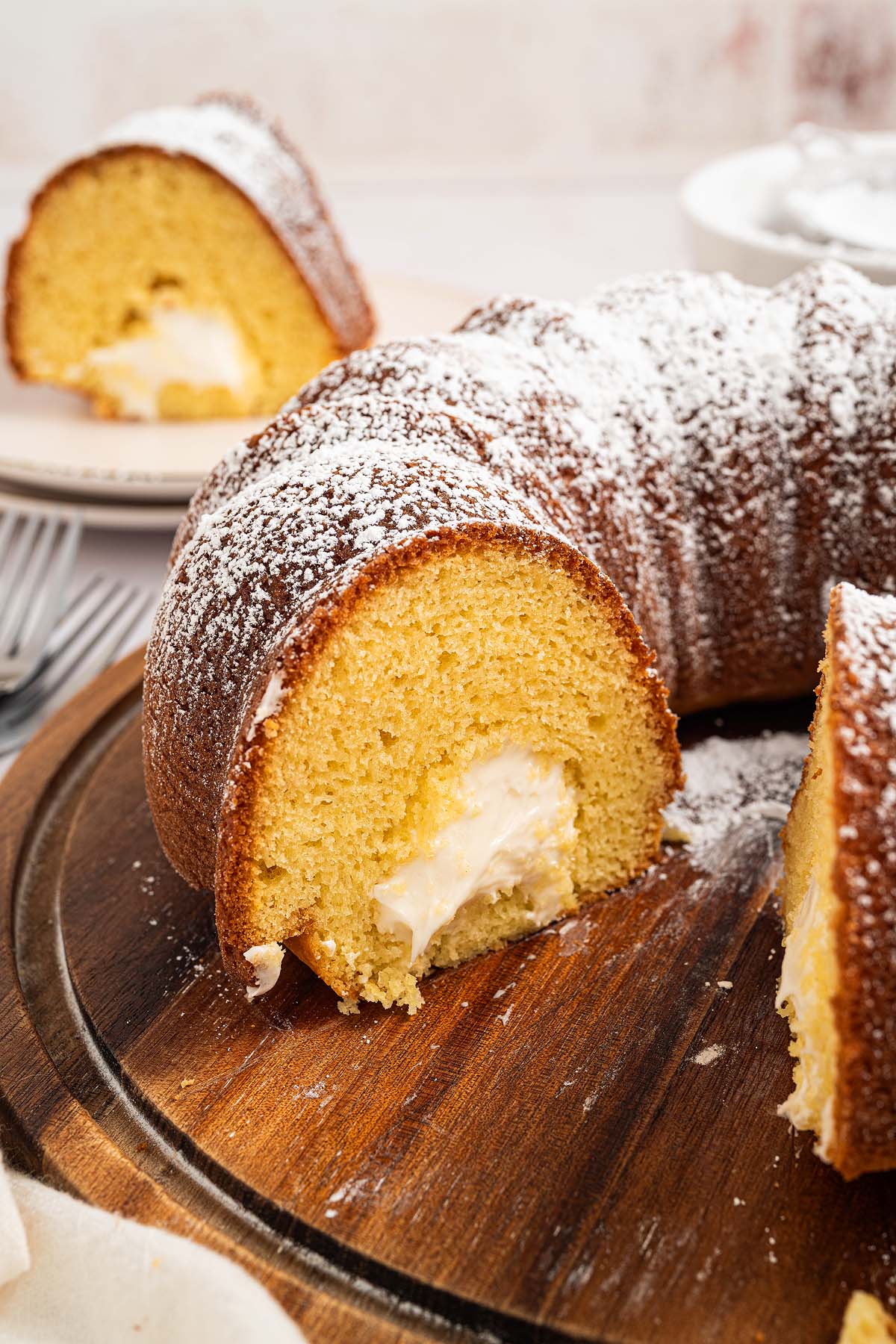 A sliced Twinkie Cake bundt with cream filling and powdered sugar on top, displayed on a wooden board.