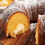 A sliced Twinkie Cake with cream filling and powdered sugar on top, served on a wooden board.