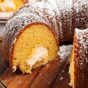 A sliced Twinkie Cake with cream filling and powdered sugar on top, served on a wooden board.