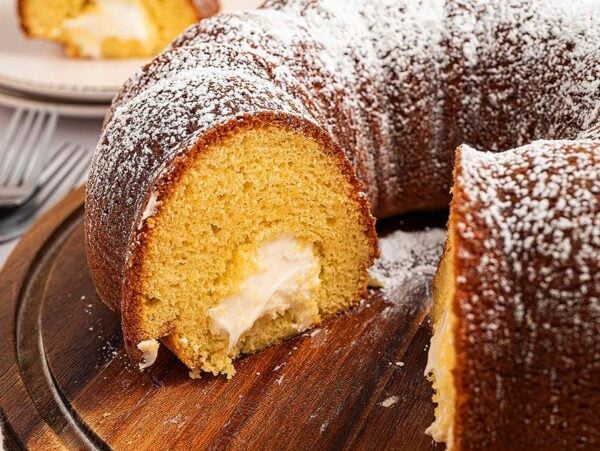 A sliced Twinkie Cake with cream filling and powdered sugar on top, served on a wooden board.