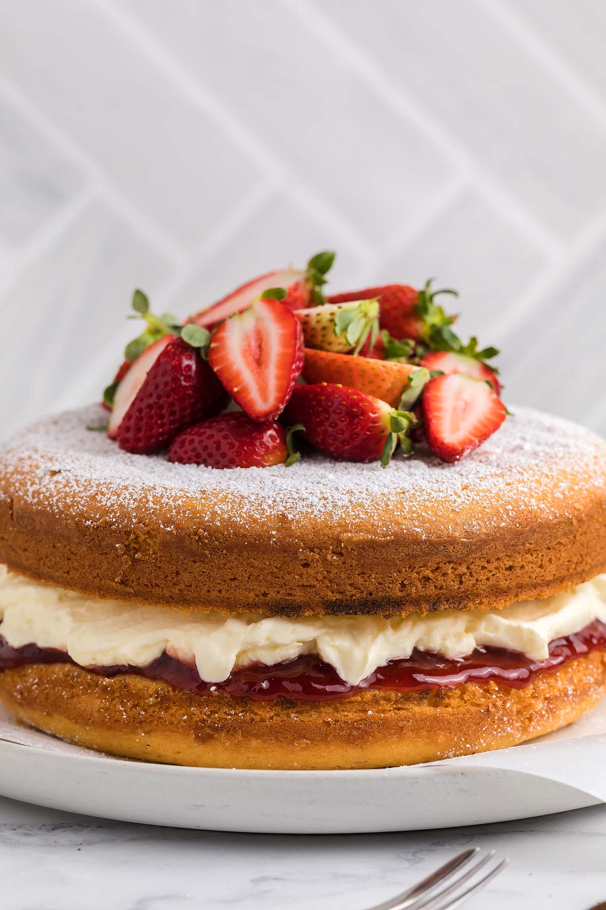 Classic Victoria Sandwich Cake with cream, jam, and fresh strawberries on top, dusted with powdered sugar.