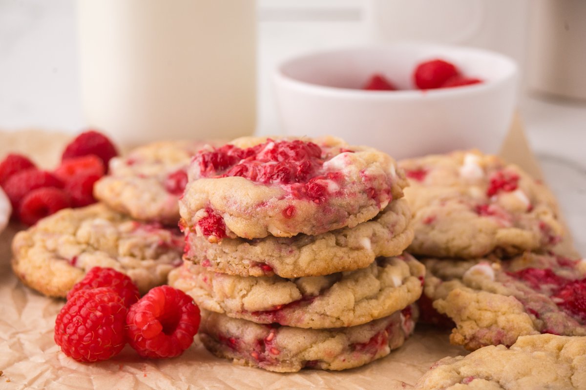 A stack of White Chocolate Raspberry Cookies with fresh raspberries and a bowl of raspberries in the background.