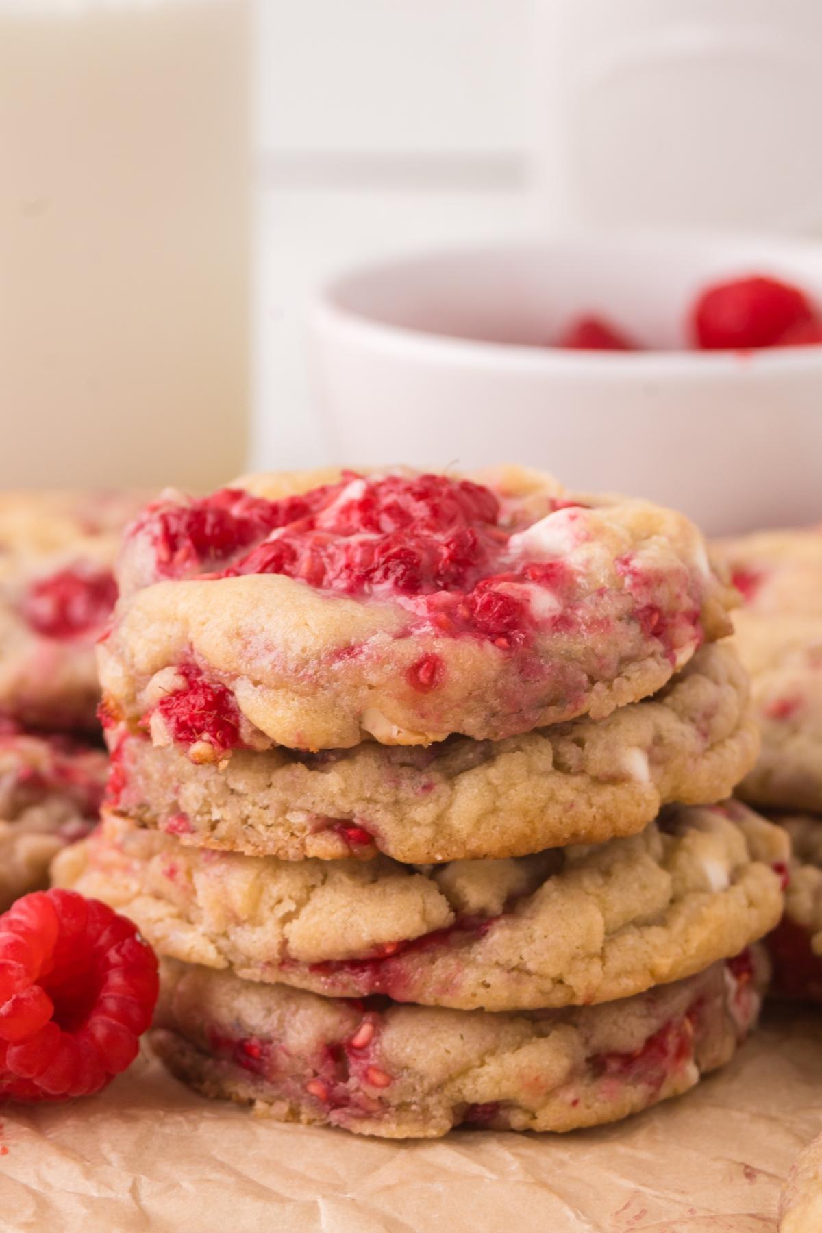 A stack of raspberry cookies with white chocolate chips, with fresh raspberries in the background.