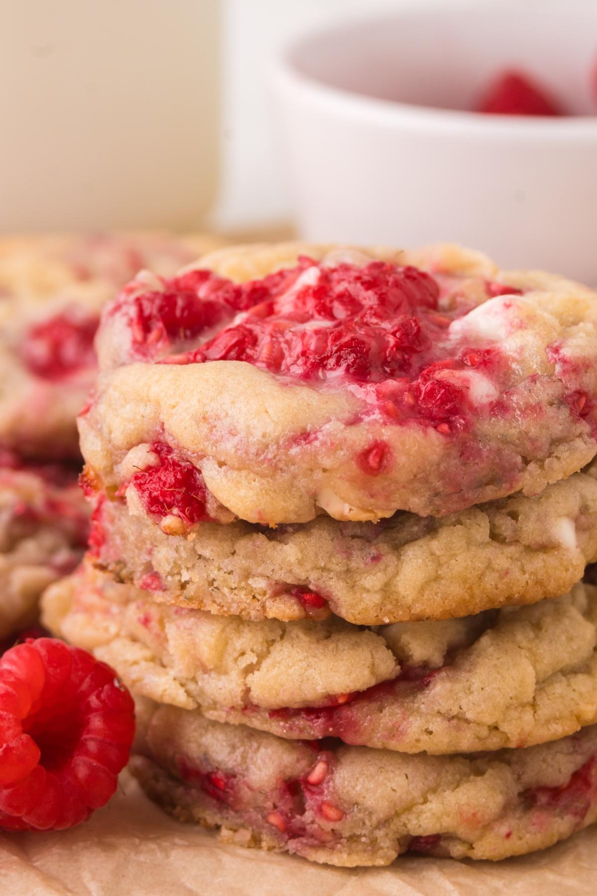 A stack of raspberry cookies with visible red berry pieces, with a fresh raspberry beside them.