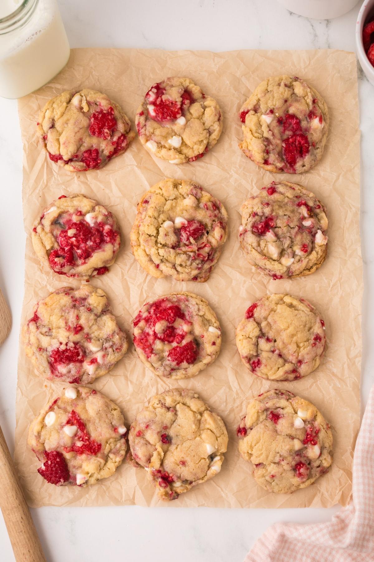 Twelve raspberry white chocolate cookies arranged on parchment paper, with a glass of milk nearby.