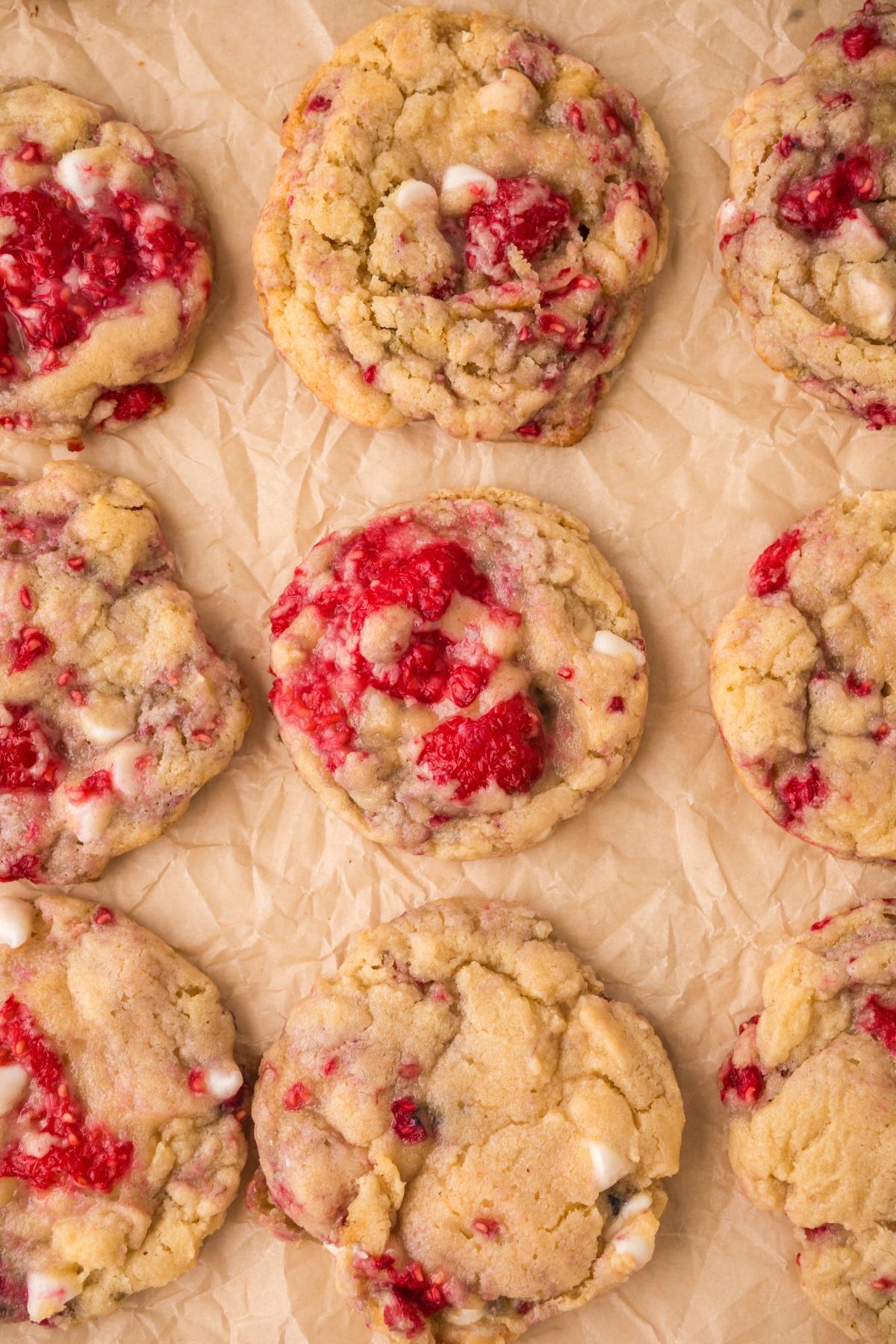 Nine raspberry white chocolate cookies arranged on crumpled parchment paper.
