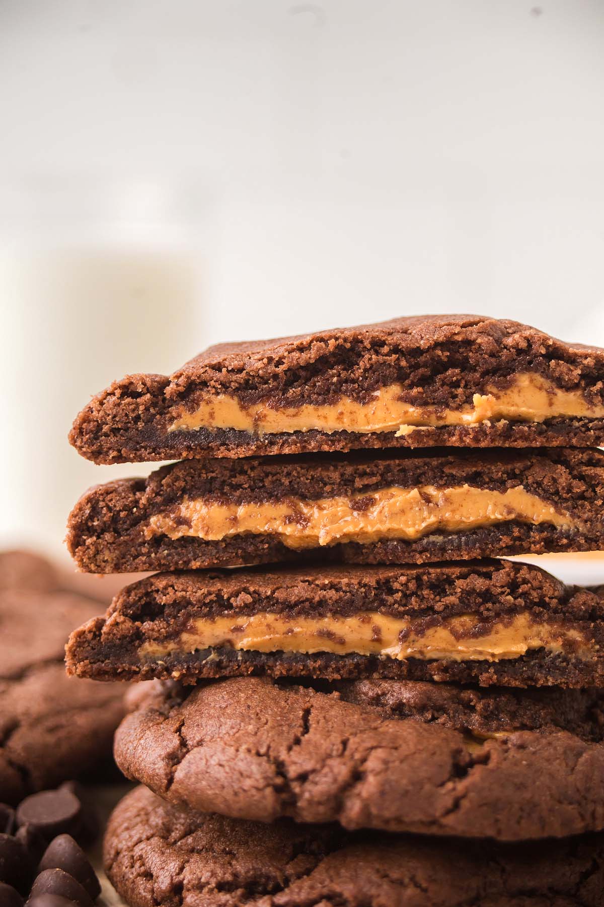 Peanut Butter Stuffed Chocolate Cookies are stacked high, showcasing their creamy peanut butter filling, with a glass of milk blurred invitingly in the background.