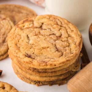 A stack of cinnamon roll sugar cookies surrounded by cinnamon sticks and a bowl of cinnamon.