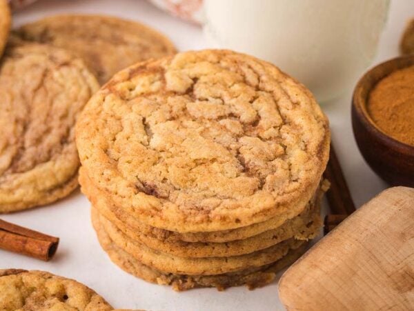 A stack of cinnamon roll sugar cookies surrounded by cinnamon sticks and a bowl of cinnamon.