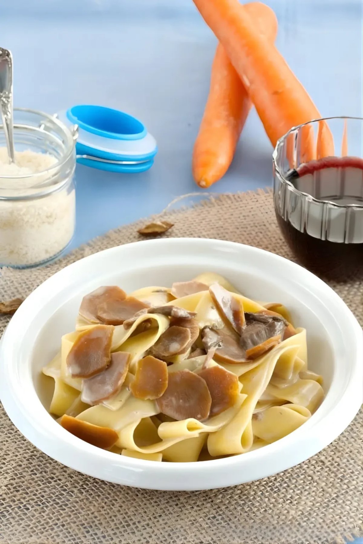 A bowl of pasta with mushrooms, next to carrots, grated cheese, and a glass of red wine—perfect for those seeking delicious Italian dinner recipes.