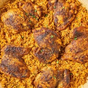 A pan of Shawarma Chicken and Rice Skillet features seasoned, baked chicken thighs atop spiced yellow rice, finished with a sprinkle of fresh herbs.