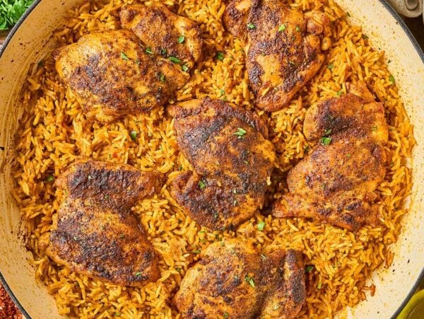 A pan of Shawarma Chicken and Rice Skillet features seasoned, baked chicken thighs atop spiced yellow rice, finished with a sprinkle of fresh herbs.
