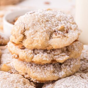 A stack of Almond Croissant Cookies, dusted with powdered sugar and filled with nuts, sits next to a glass of milk on the table.