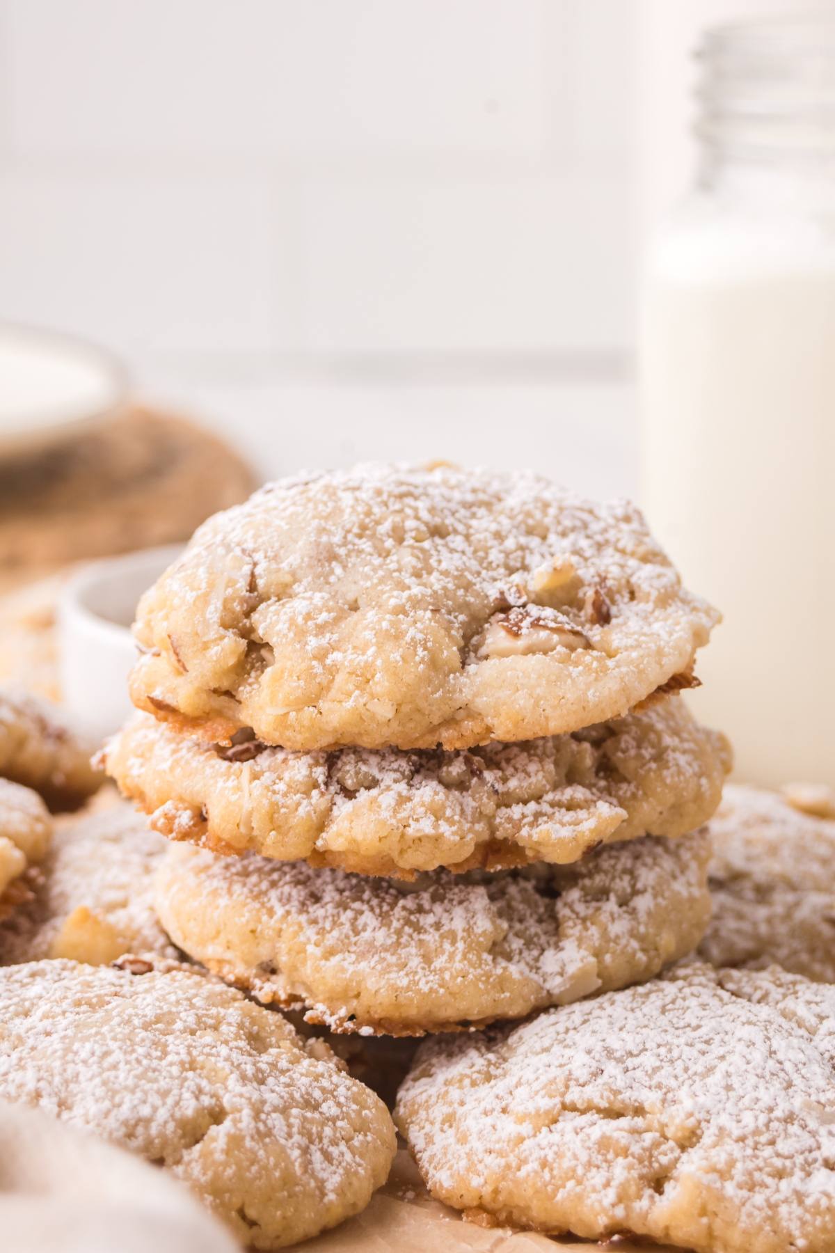 A stack of powdered sugar-dusted cookies with a glass of milk in the background.