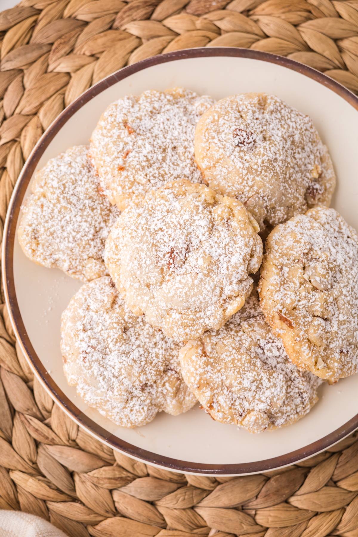 A plate of seven powdered sugar-dusted cookies on a woven placemat.