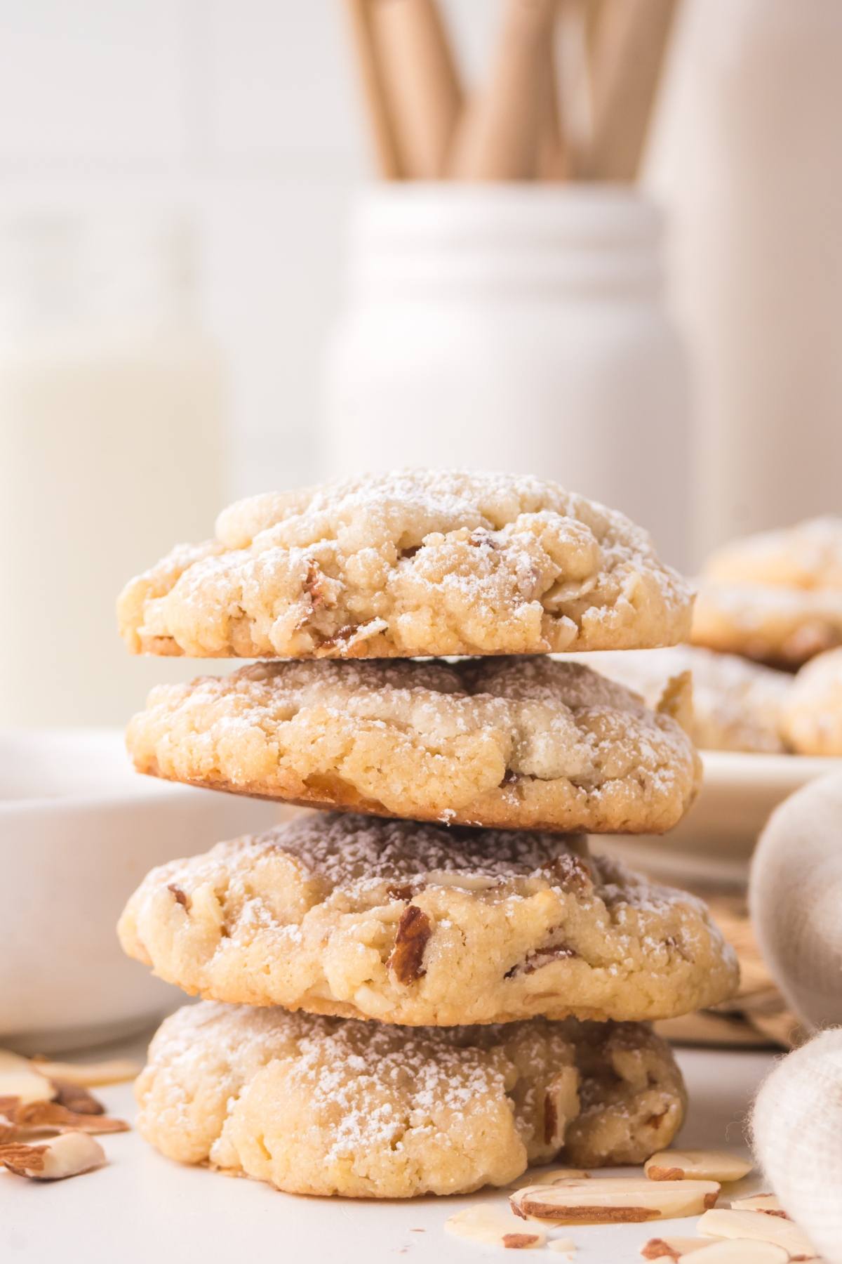 Four almond cookies stacked on top of each other, dusted with powdered sugar, on a white surface.
