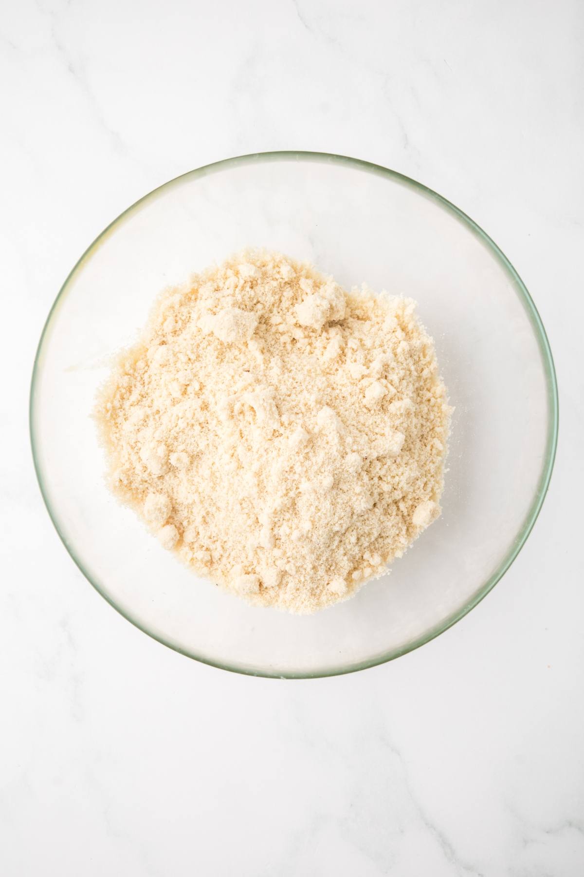 A glass bowl filled with finely ground almond flour on a white surface.