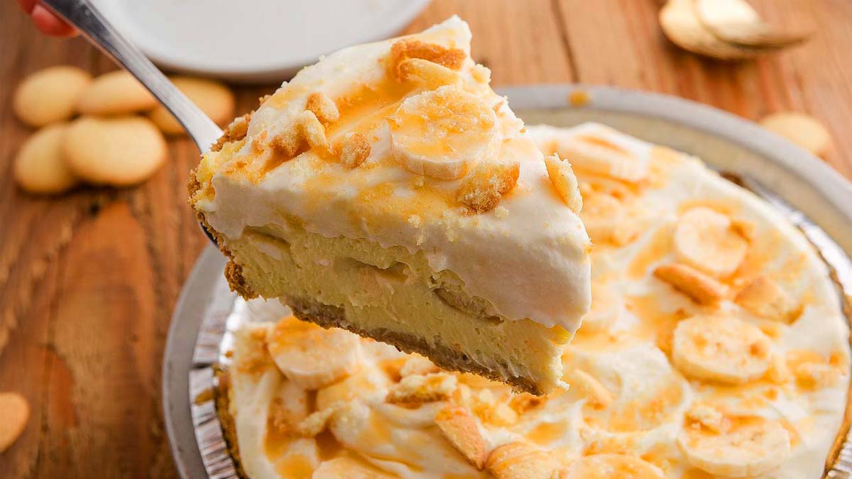 A slice of creamy Banana Pudding Pie with whipped topping and cookie pieces is lifted from the whole pie.