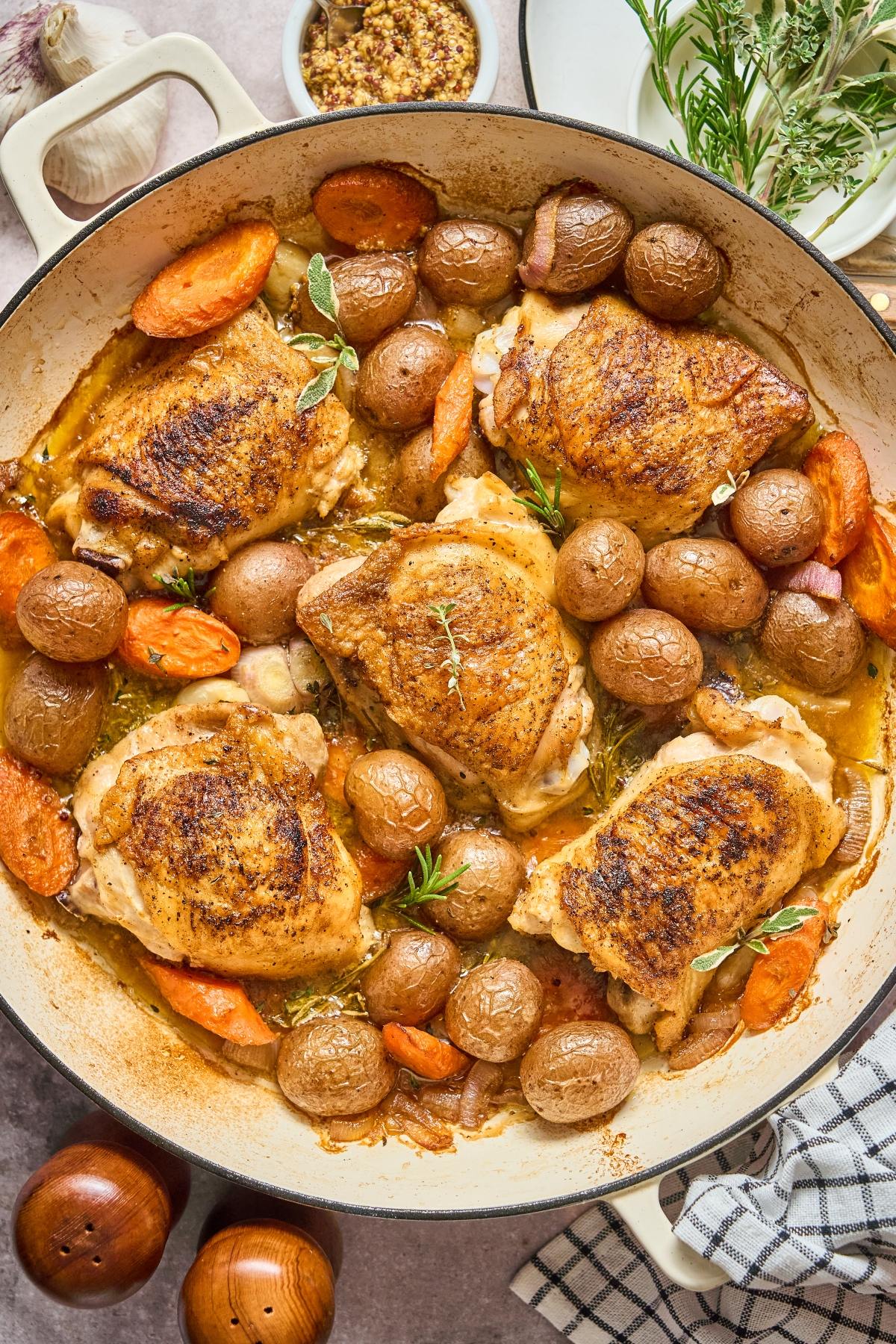 Roasted chicken thighs with baby potatoes and carrots in a large skillet, garnished with fresh herbs.