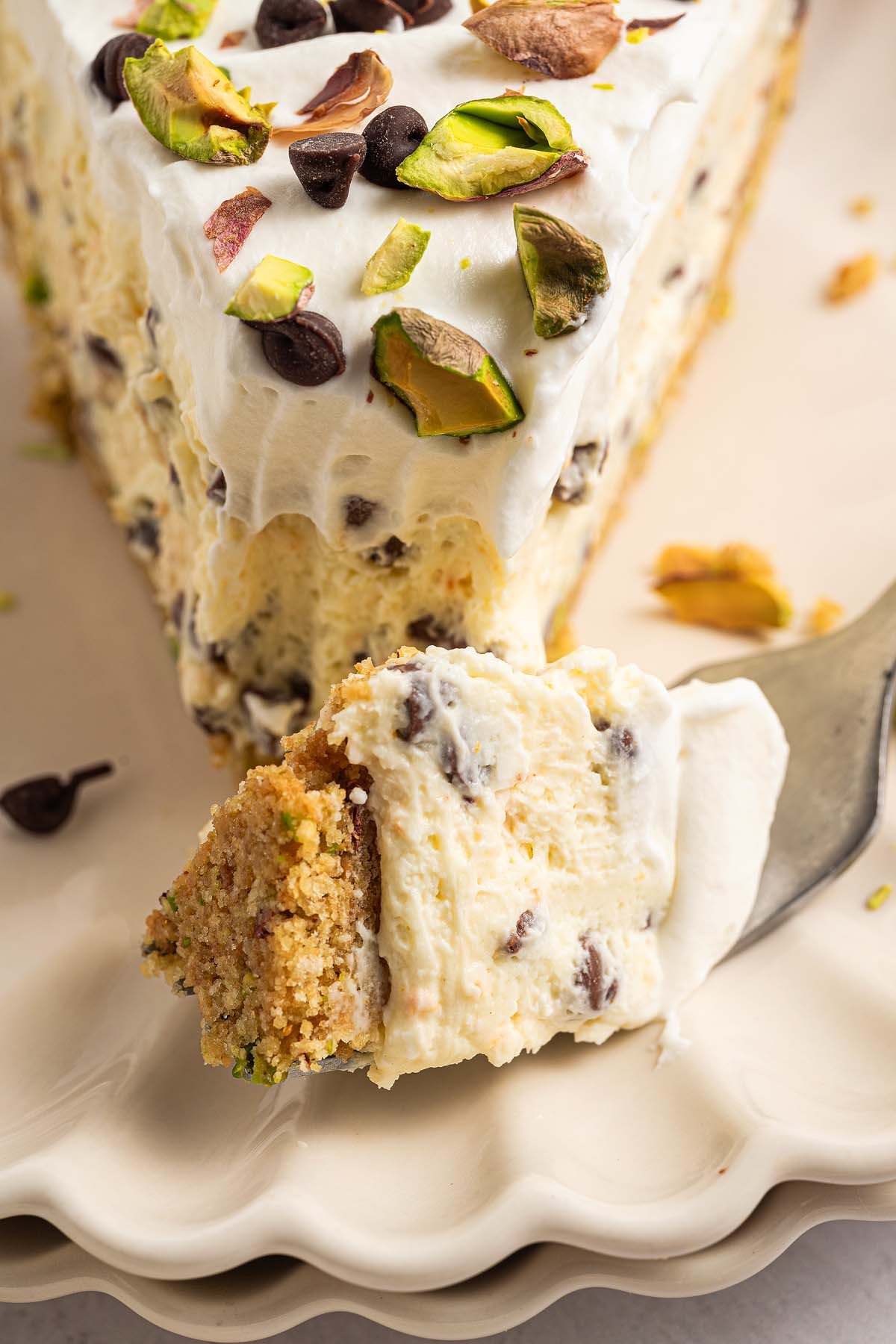 A slice of creamy Cannoli Pie cheesecake with chocolate chips and pistachios on top, with a bite on a fork.