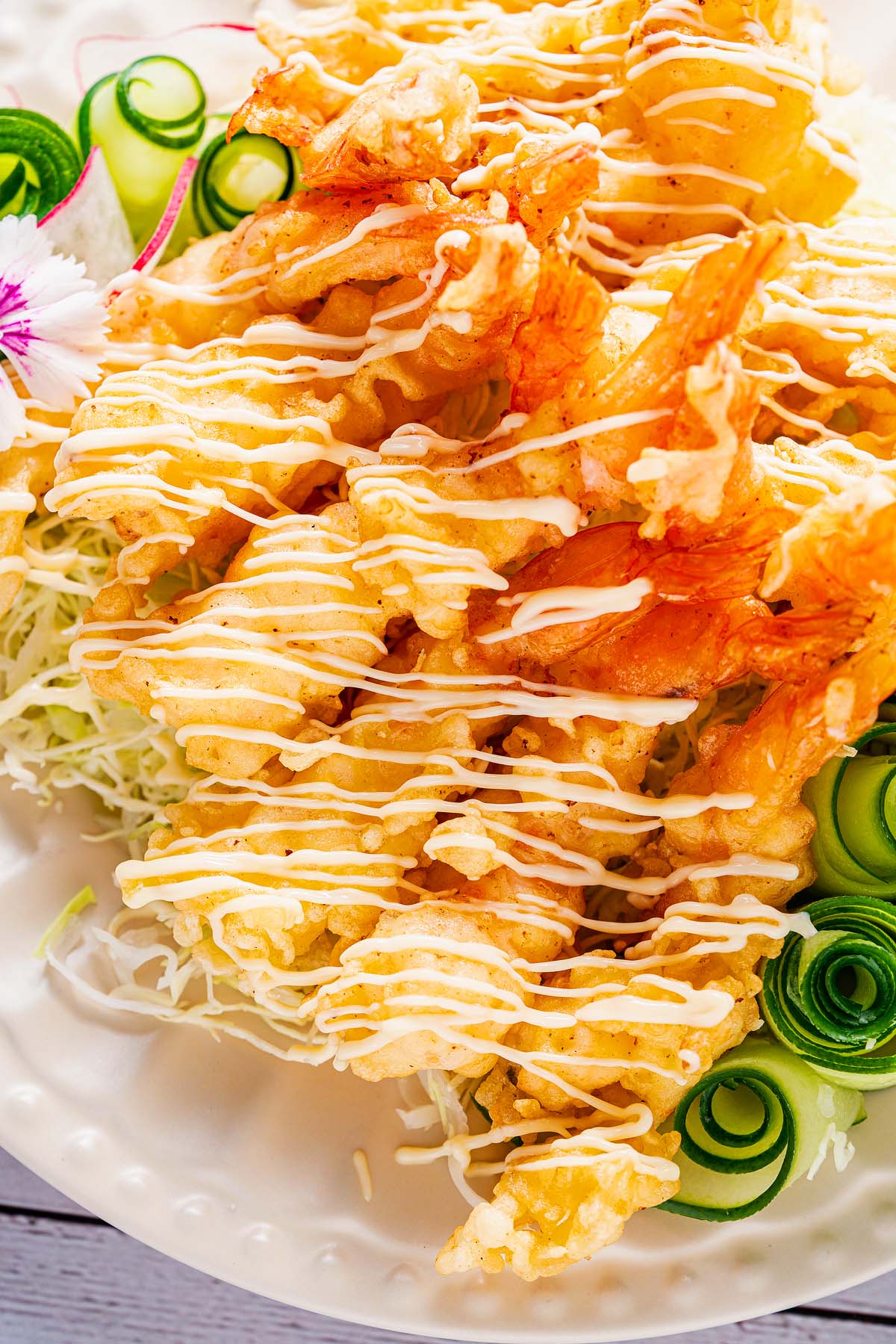 Golden fried shrimp tempura drizzled with sauce, served atop shredded cabbage and garnished with crisp cucumber spirals.