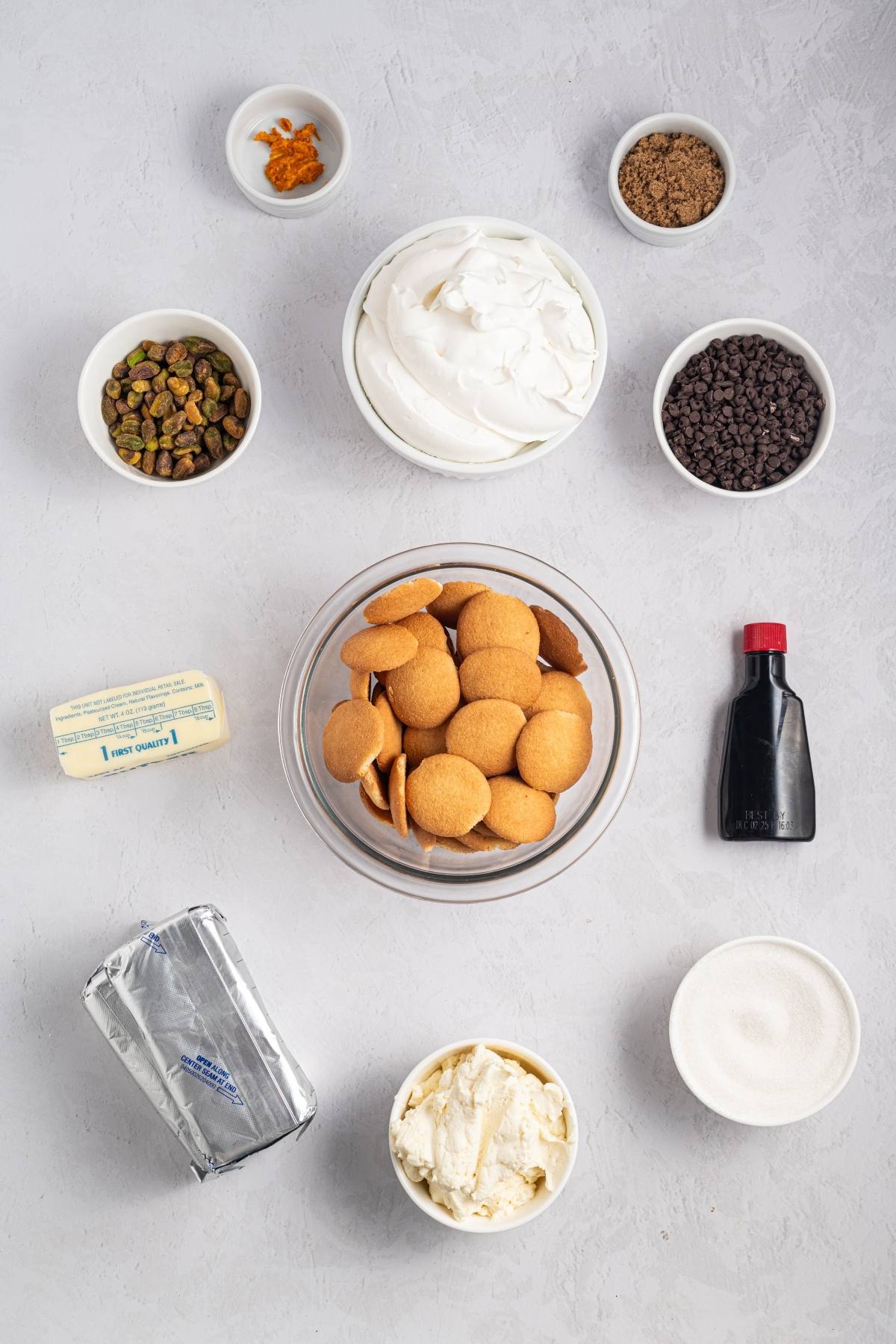 Various dessert ingredients, including wafers, whipped topping, chocolate chips, nuts, and dairy, arranged on a gray surface.