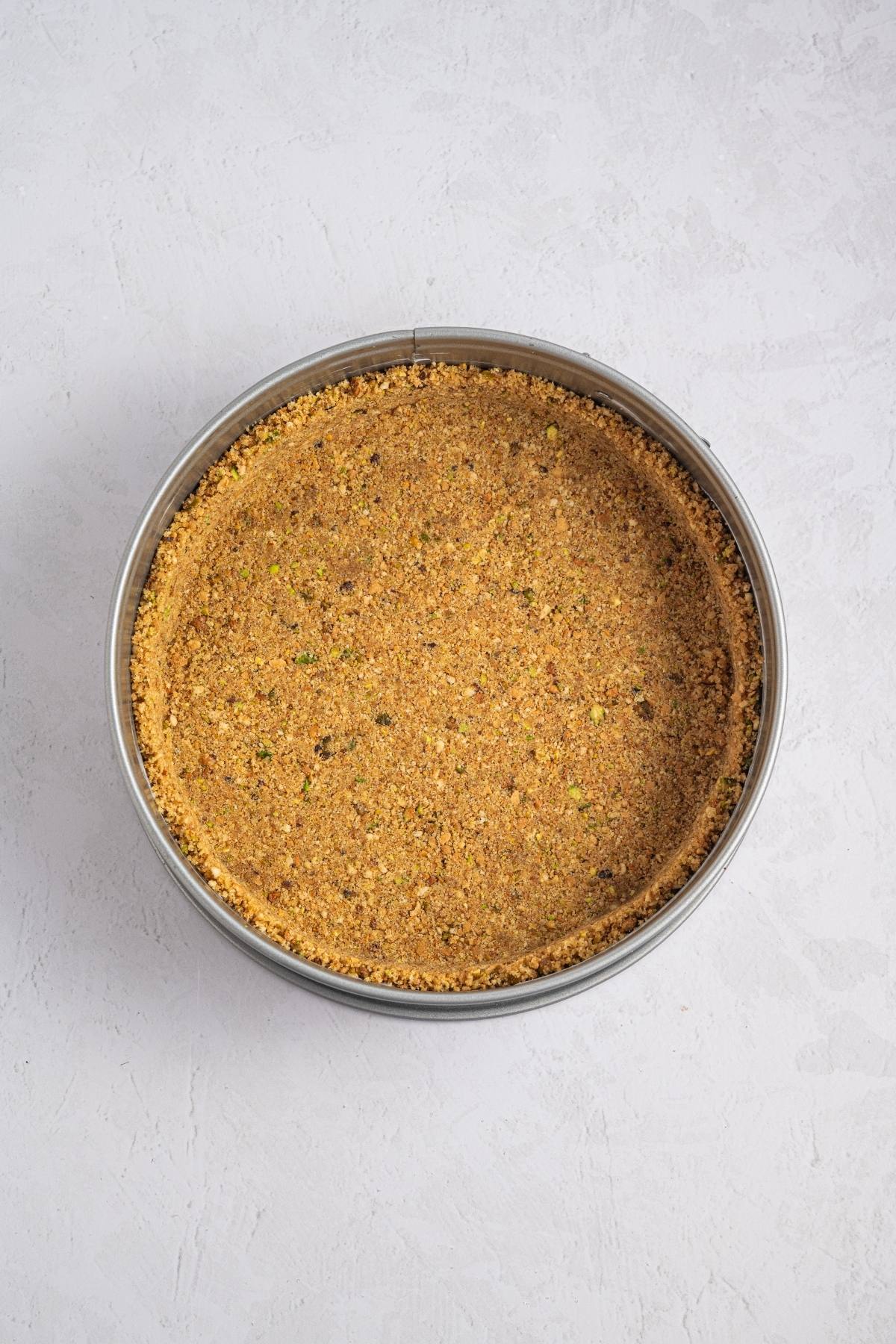 A round pan with a pressed graham cracker crust on a light textured surface.