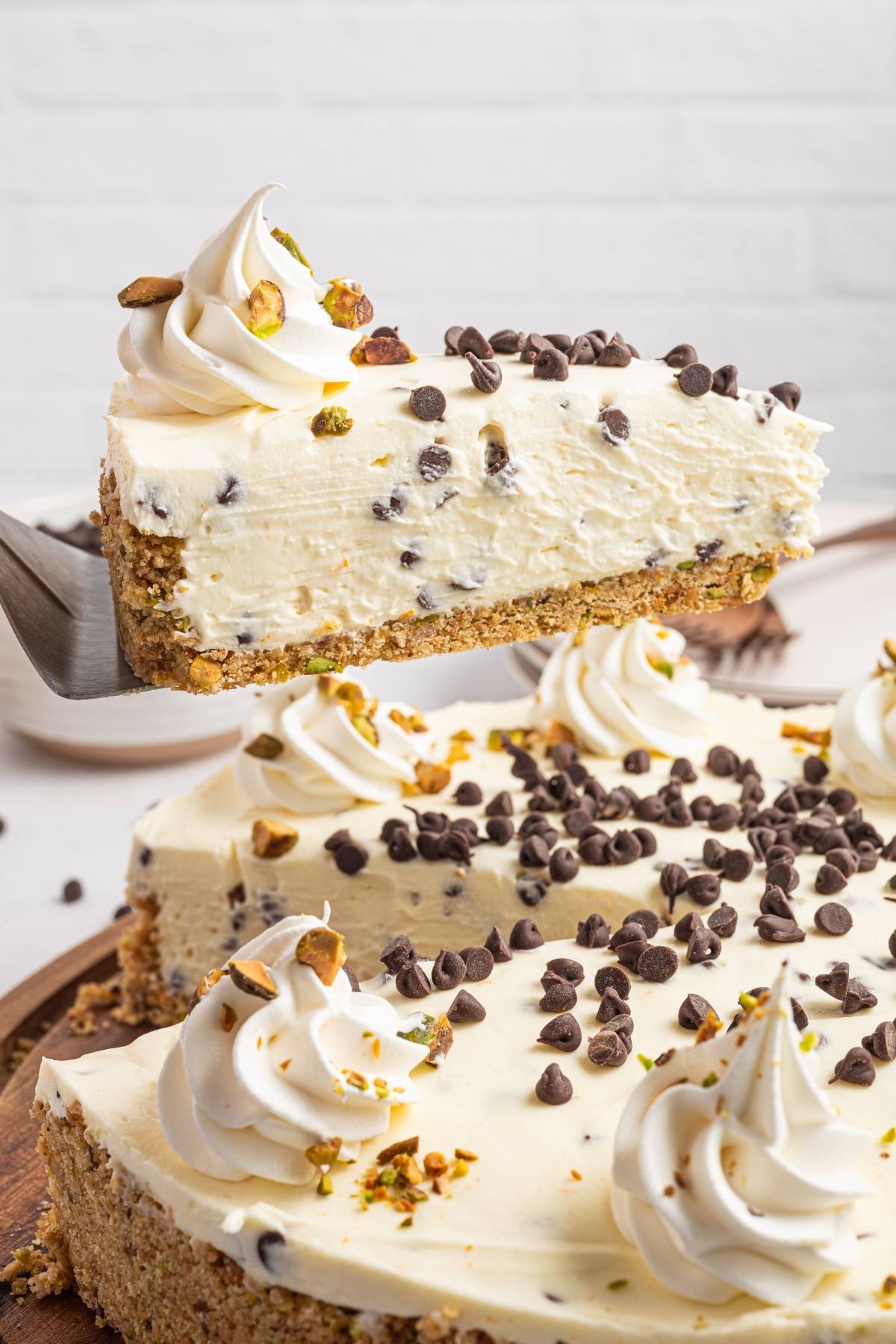A slice of cannoli cheesecake with chocolate chips and whipped cream being lifted from a whole cheesecake.
