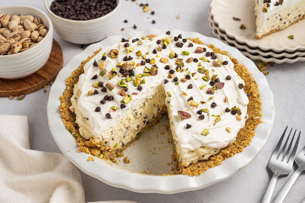 Creamy Cannoli Pie topped with whipped cream, chocolate chips, and chopped pistachios, with a slice removed.
