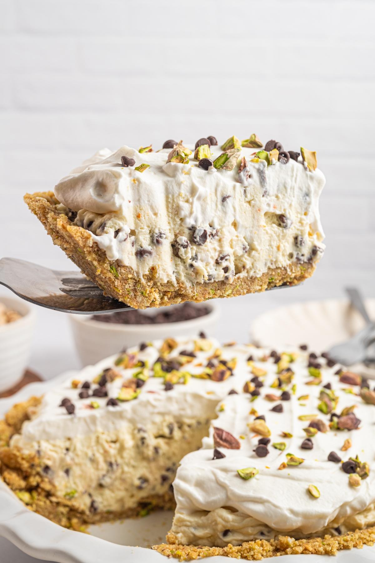 A slice of creamy pie with chocolate chips and pistachios being lifted from a pie dish.