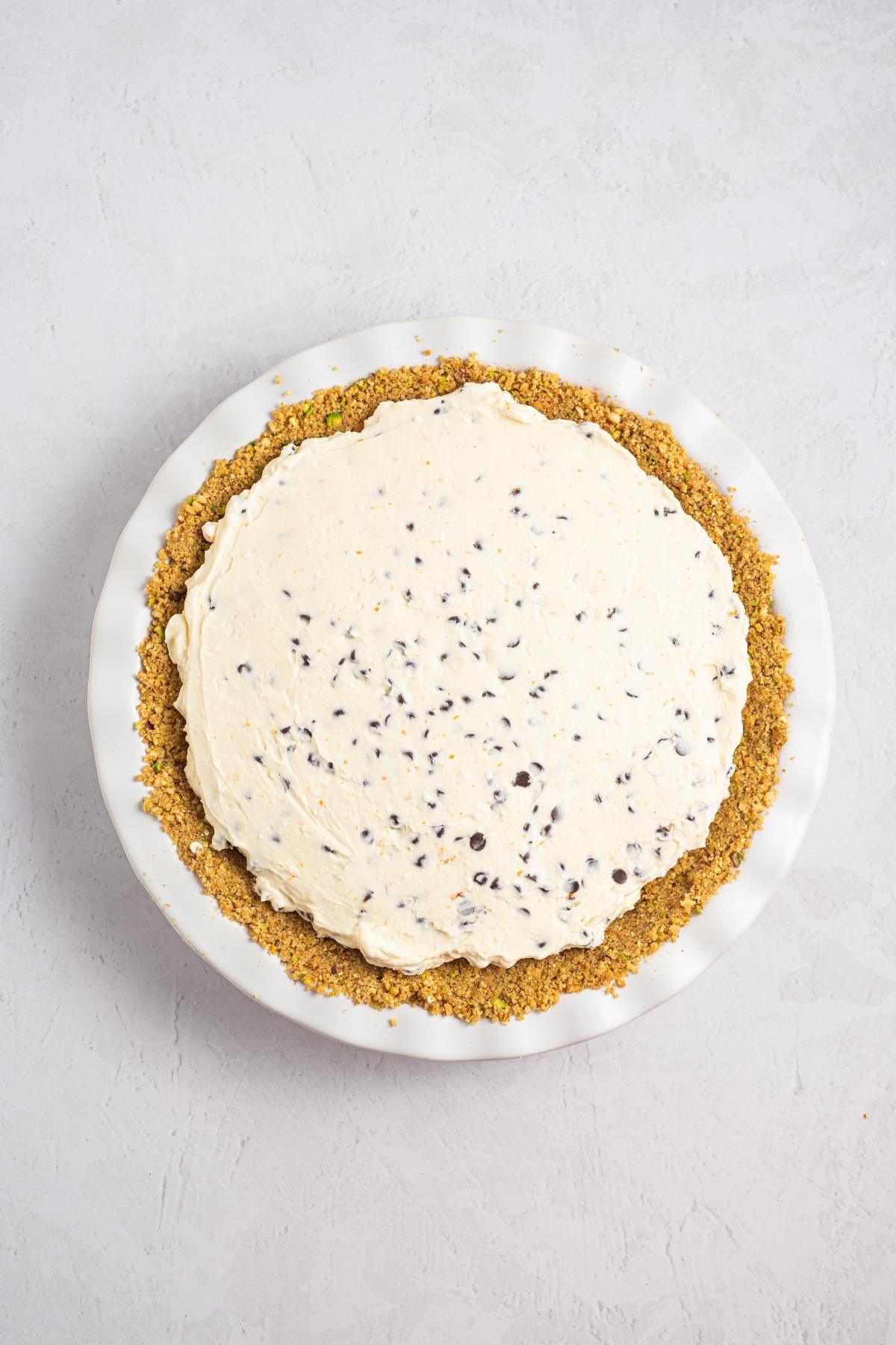 A pie with a graham cracker crust and a creamy filling with chocolate chips, in a white pie dish.