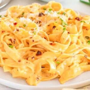 Creamy Chili Crisp Fettuccine Alfredo topped with grated cheese and fresh green herbs on a white plate.